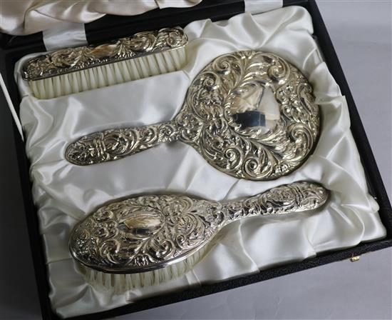 A cased modern three piece repousse silver mirror and brush set, Birmingham, 1977